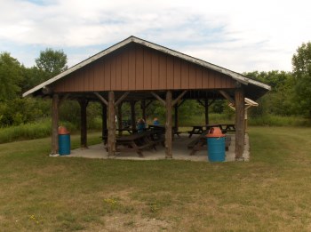 Brown wooden pavilion with several picnic tables and garbage cans. 