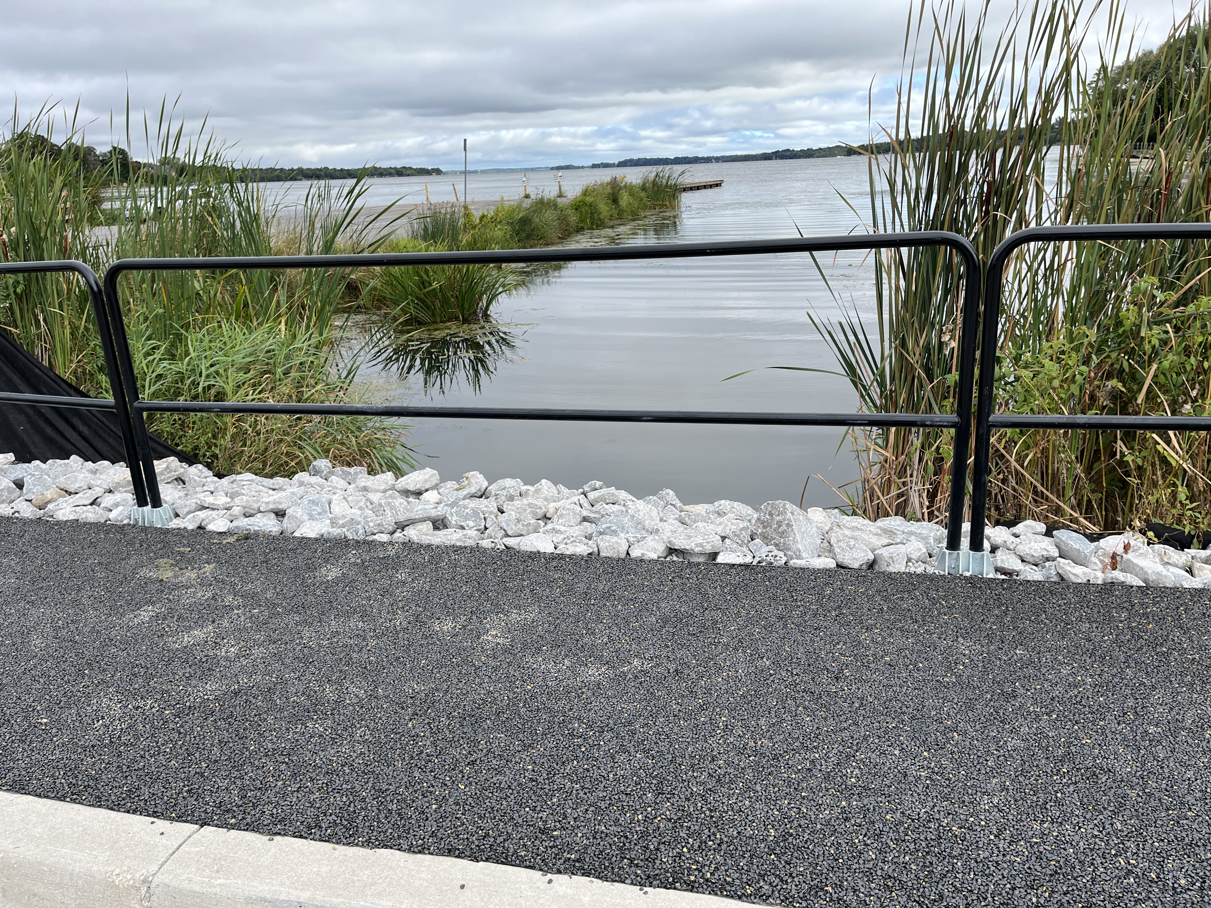 Grey permeable pavement pathway adjacent to railing looking out over Lake Scugog.
